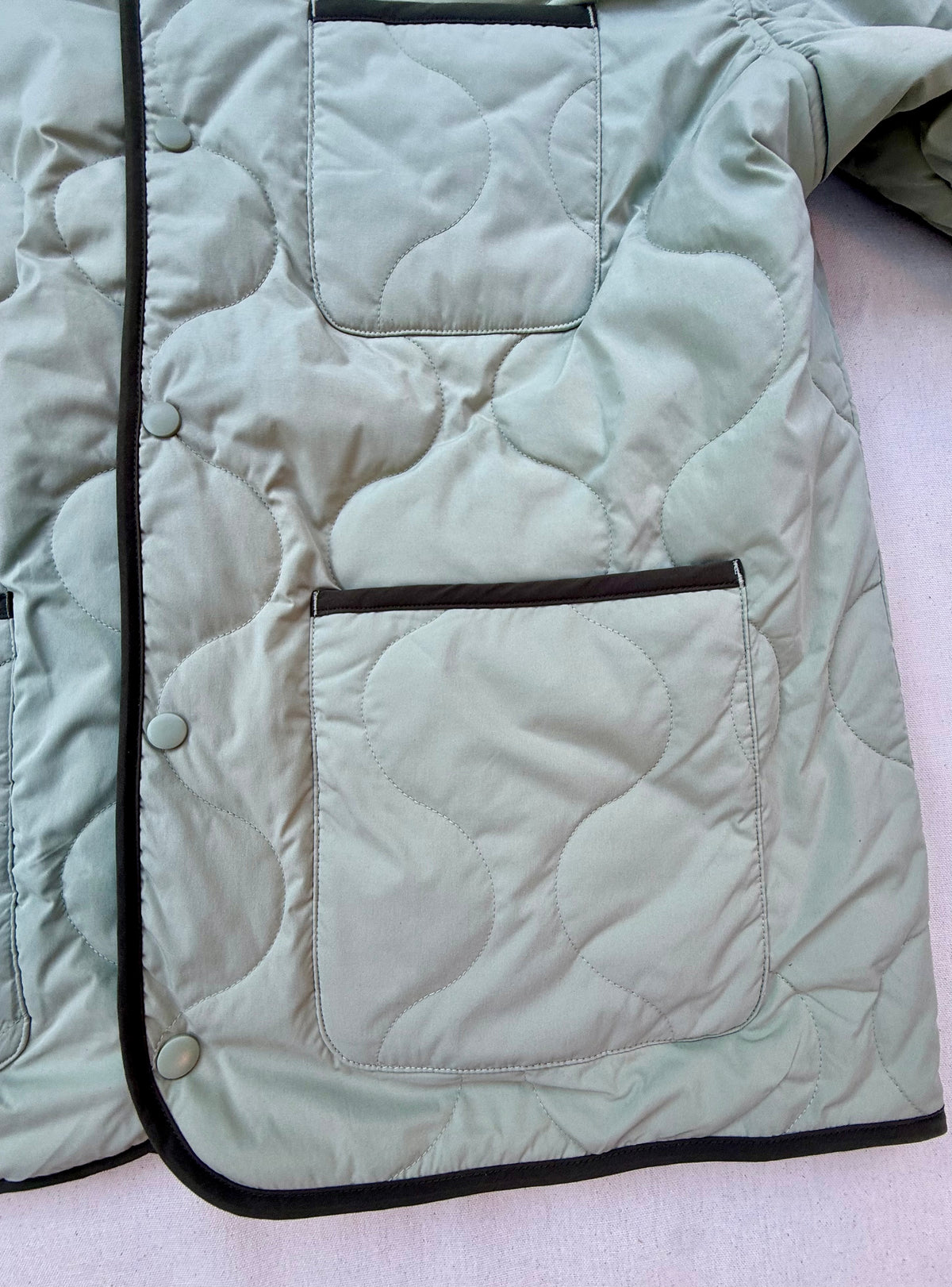 Close-up of sage quilted jacket pockets with olive trim and snap buttons