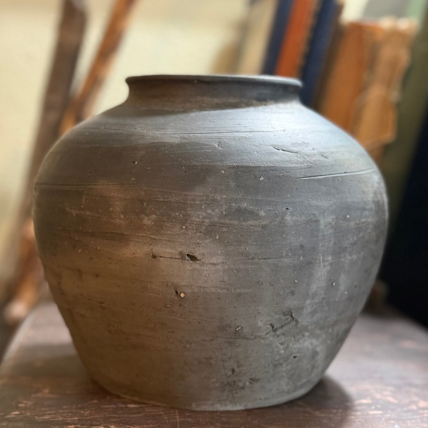 This is a vintage, unglazed clay pot or vessel, likely originating from China's Shanxi province, used historically for storing dry goods. 

	•	The pot is handcrafted with a rounded silhouette and a textured, weathered gray finish.  
	•	The unglazed earthenware has an aged patina, with signs of age and wear that add to its character.  
	•	It is a decorative accent item, typically not water safe for use with fresh flowers. 
