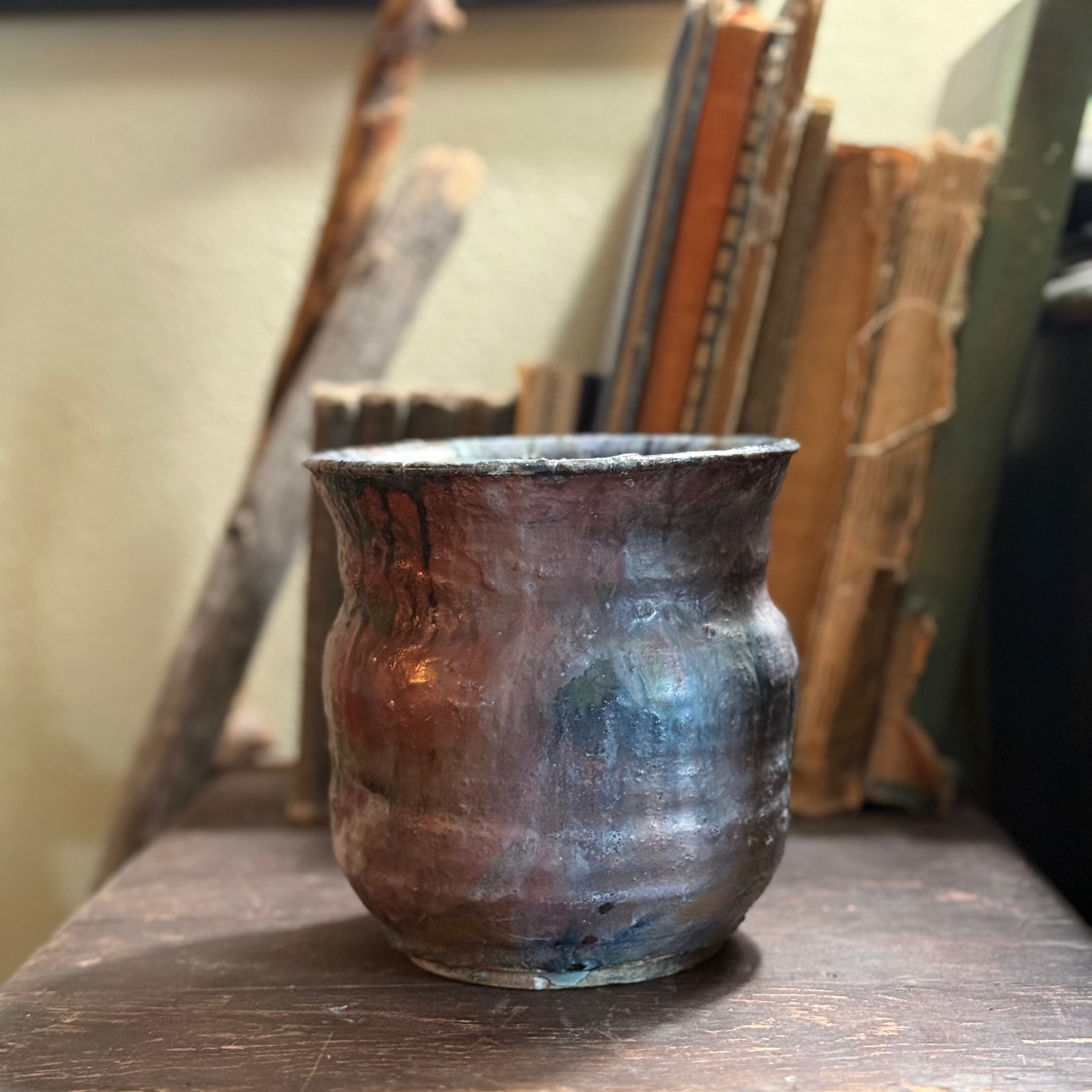 Ceramic pot on a wooden surface with books and branches in the background