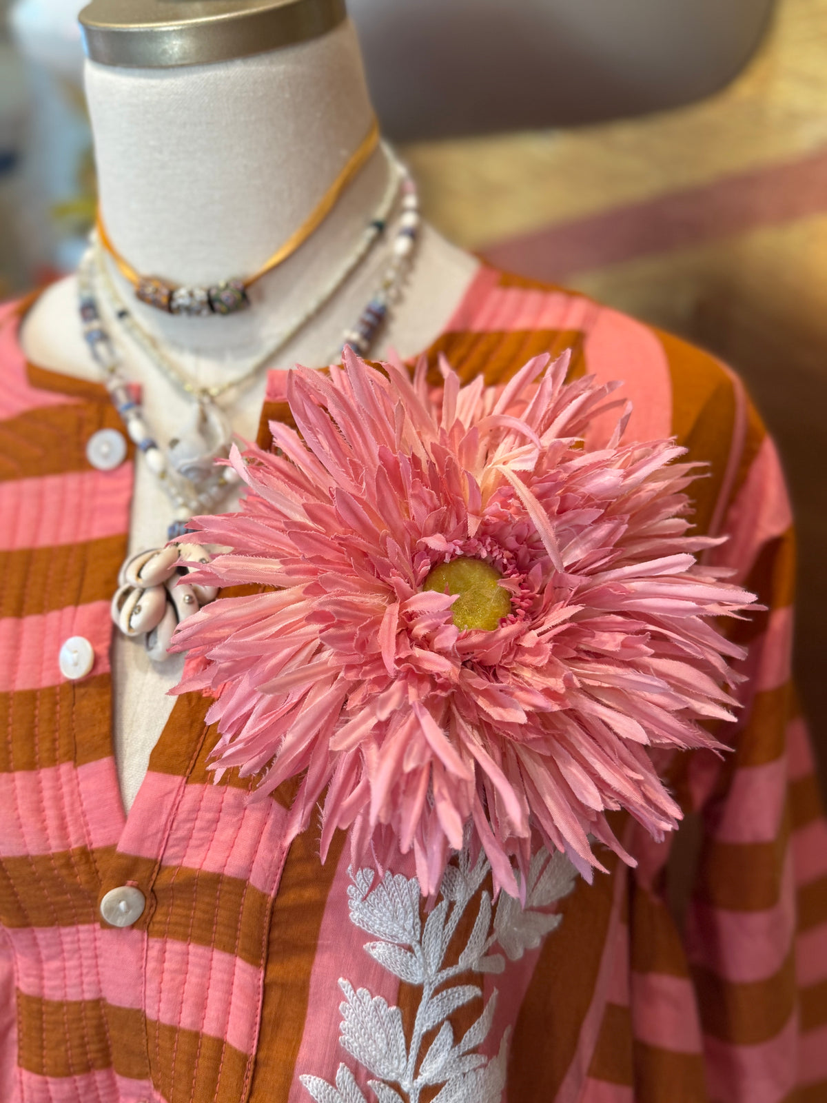 Pink spider mum flower pin on a pink and brown striped top with layered necklaces