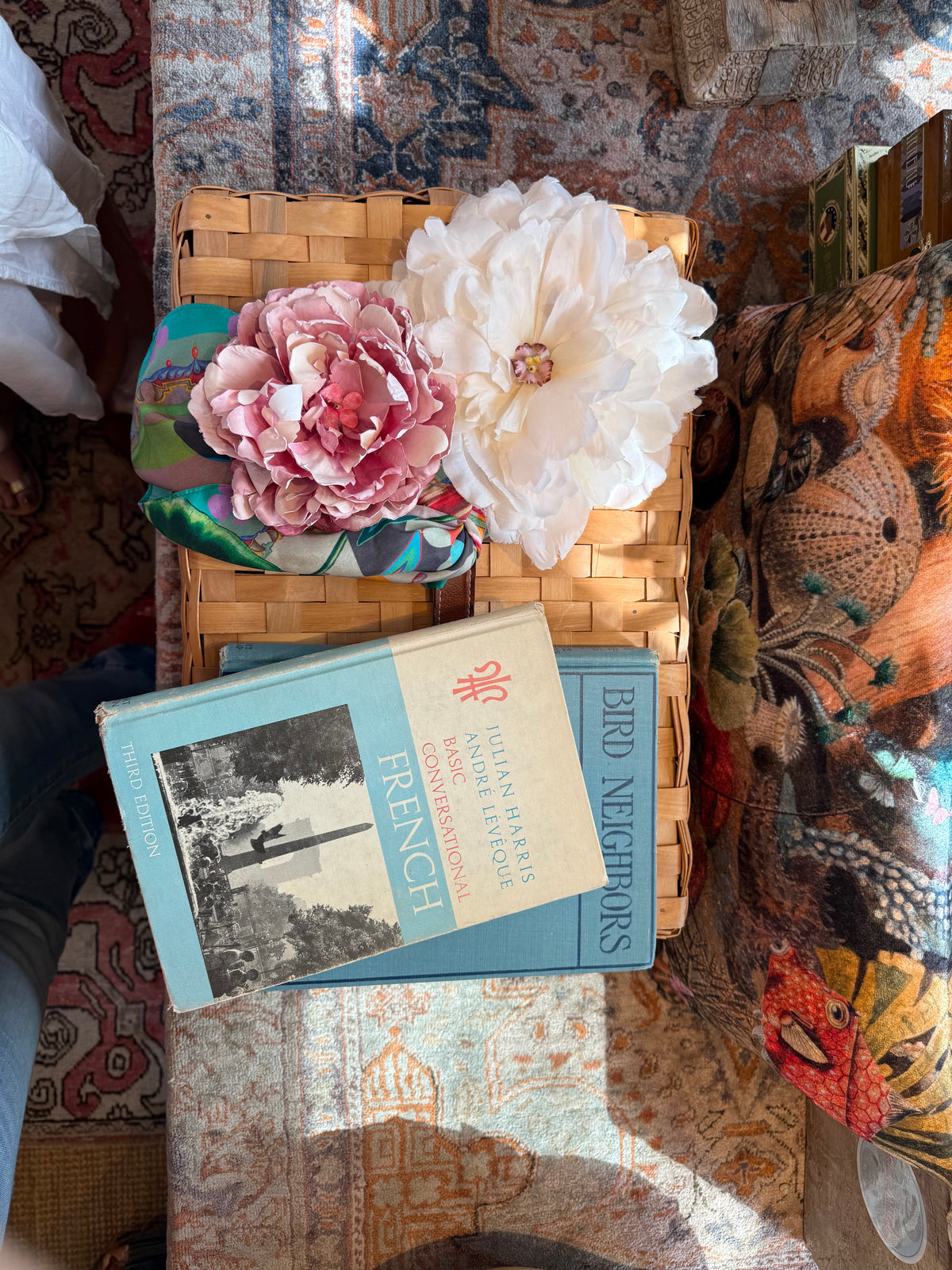 Pink and white peony flower pins with a silk scarf on a wicker basket, beside vintage books