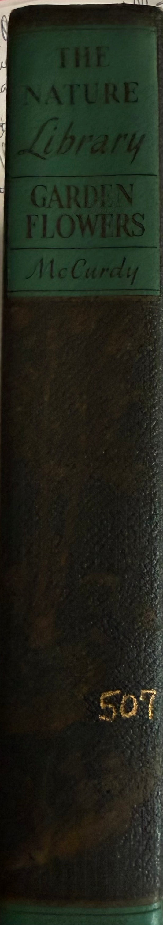 A close-up of a vintage book spine titled 'The Nature Library Garden Flowers' by McCurdy, with a dark brown leather-like cover and a green title block.
